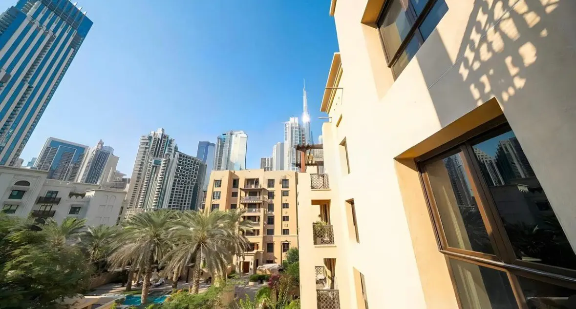 View of Dubai skyline with Burj Khalifa, palm trees, and beige buildings under a clear blue sky.
