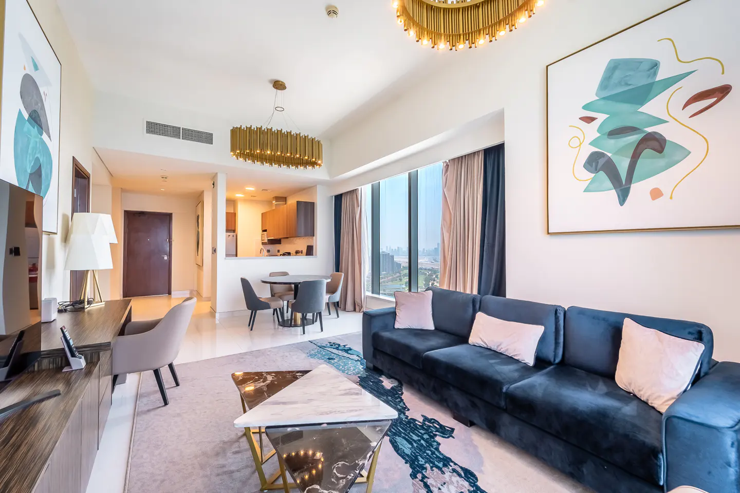 Modern living room with a navy sofa, pink pillows, marble coffee table, and dining area with a view of the city skyline.