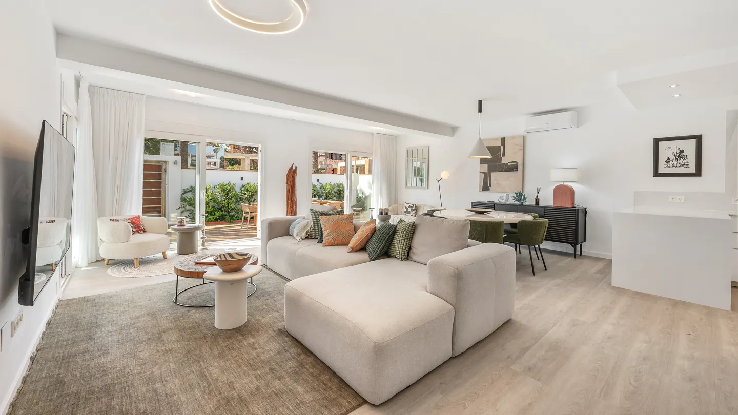 Bright living room with a beige sectional sofa, round dining table with green chairs, and sliding glass doors to a patio.
