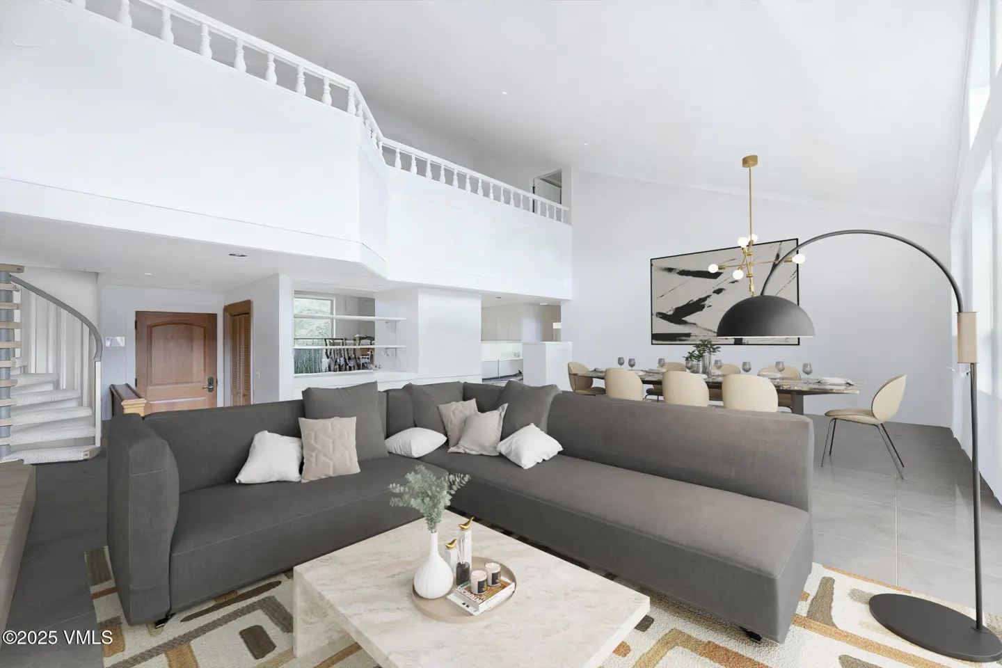Bright, modern living room with a gray sectional sofa, marble coffee table, and dining area. White walls and a spiral staircase add to the airy feel.