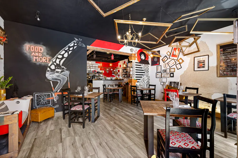 Eclectic restaurant interior with wooden tables, black chairs, and artful wall murals. Empty gold picture frames hang from the black ceiling.