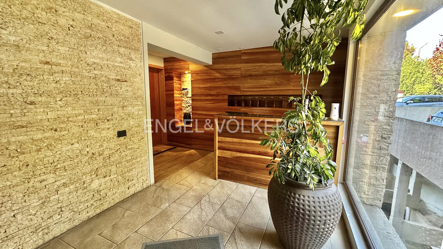 A real estate office lobby with stone and wood walls, tile floors, and a large potted plant by a window.