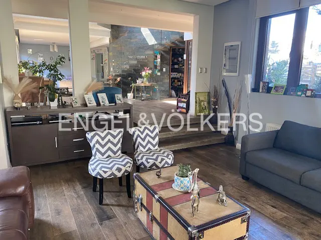 Open-concept living room with wood floors, gray sofa, and chevron chairs. A trunk serves as a coffee table. Stairs lead to another room.
