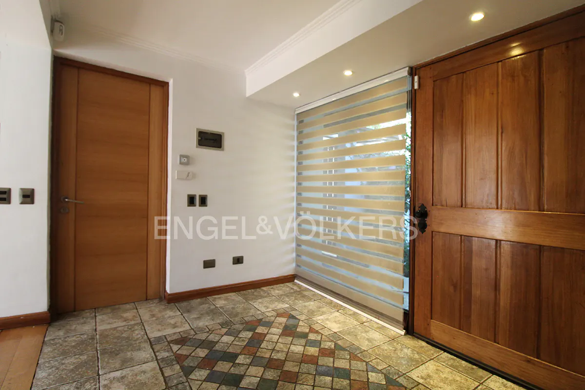 Entryway with a wooden door, a striped blind, and a tiled floor. The walls are white, and the Engel & Völkers logo is visible.