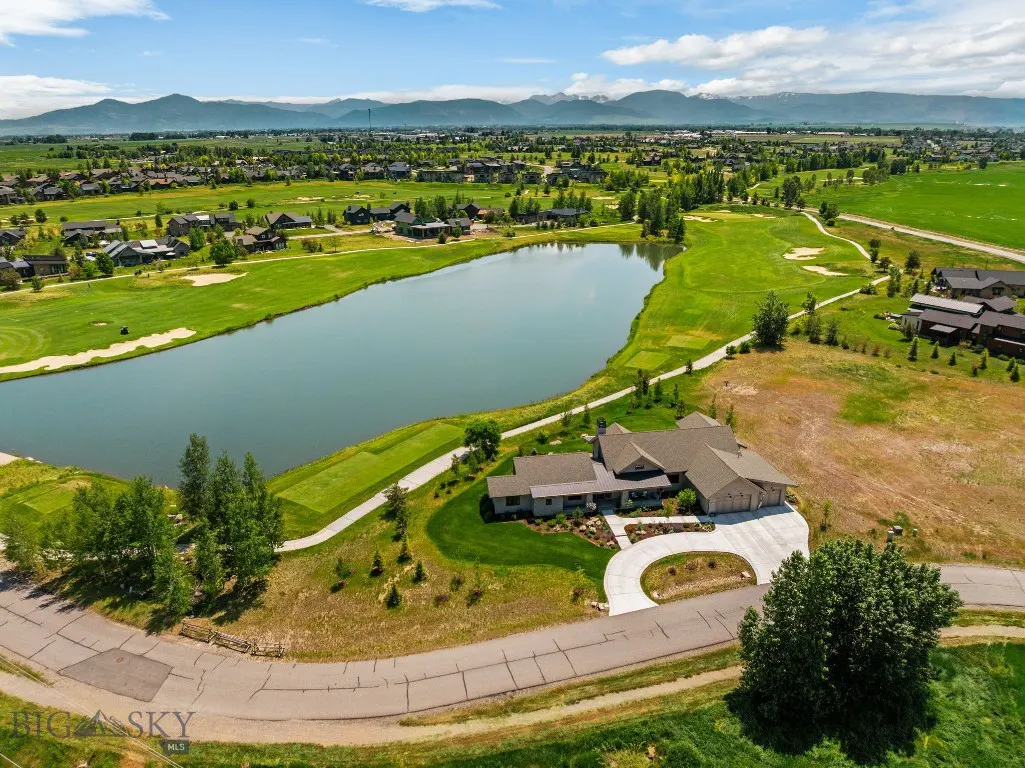 Aerial view of a luxury home on a golf course with a lake, green grass, and mountains in the background.