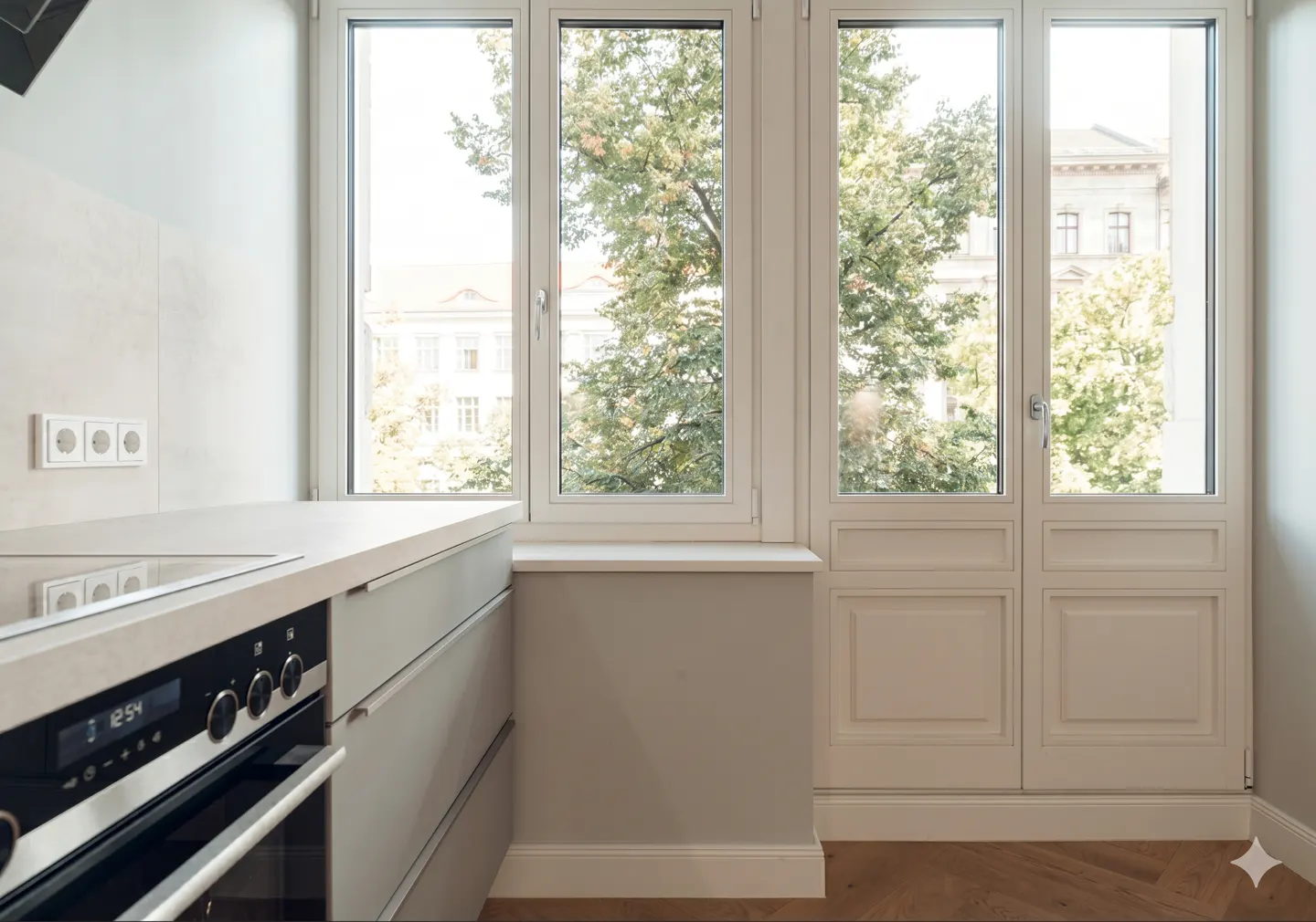 A bright kitchen corner with a white countertop, oven, and a large window showing trees and a building.