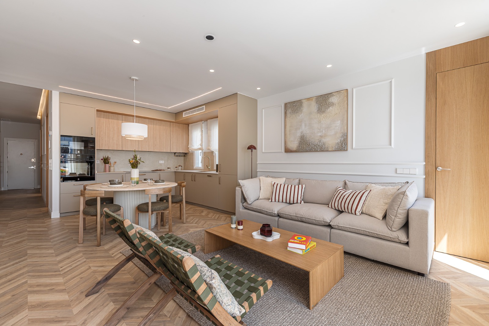 Modern open-plan living room with beige sofa, wooden coffee table, dining area, and herringbone wood floors.