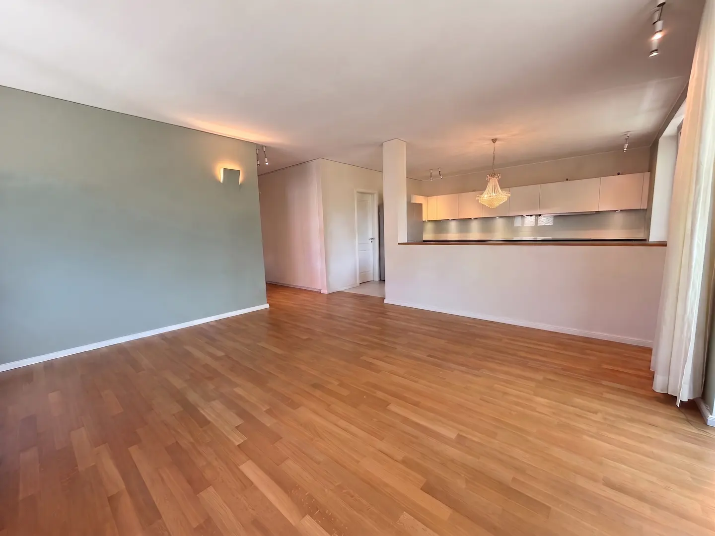 Open-concept living space with hardwood floors, a sage green accent wall, and a kitchen with white cabinets and a chandelier.