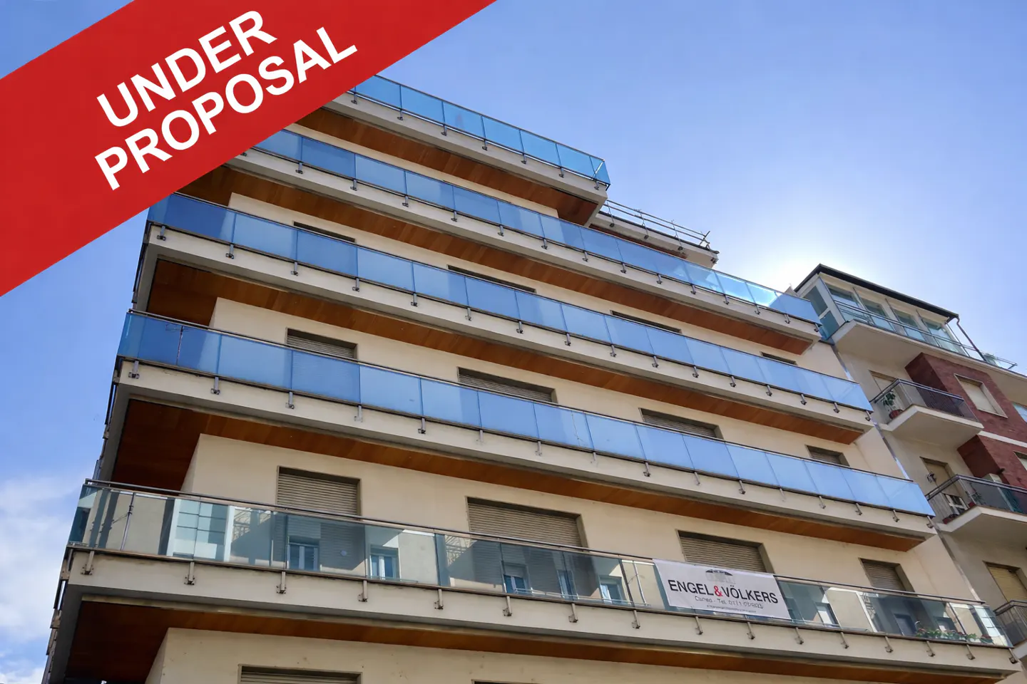 Exterior view of a modern apartment building with blue glass balconies under a blue sky. A red banner reads "Under Proposal".