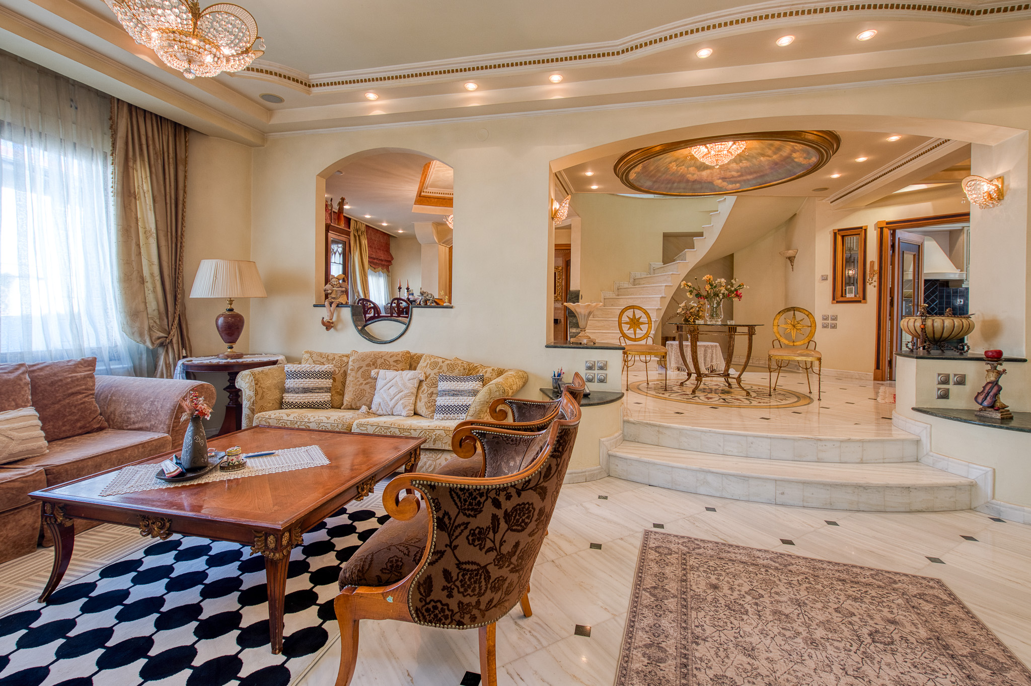 Luxurious living room with ornate furniture, a wooden coffee table, and a marble staircase leading to an upper level.