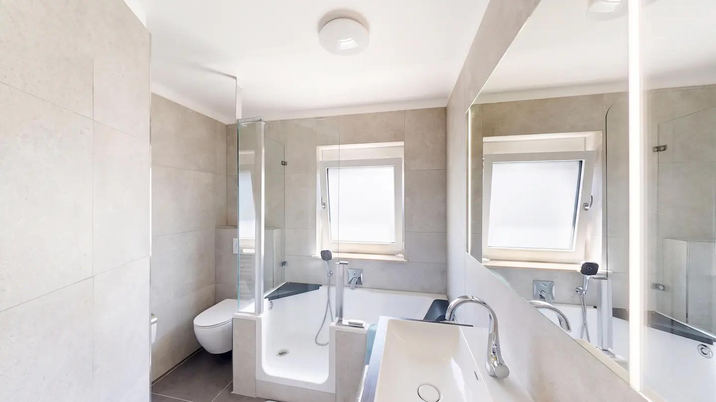Modern bathroom with beige tiled walls, a walk-in shower with a glass door, a white toilet, and a vanity with a mirror.