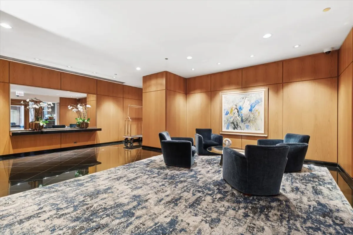 Lobby with wood paneled walls, black marble floor, and blue armchairs on a patterned rug. Artwork hangs on the wall.