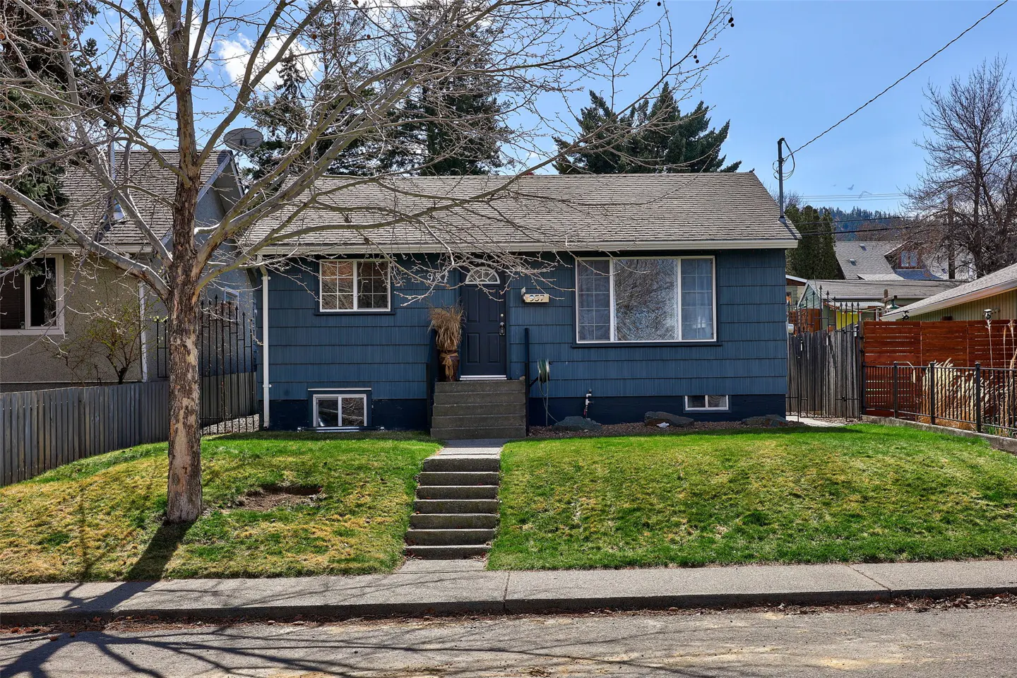 A blue, single-story house with a gray roof and a small front yard with green grass. Concrete steps lead to the front door.