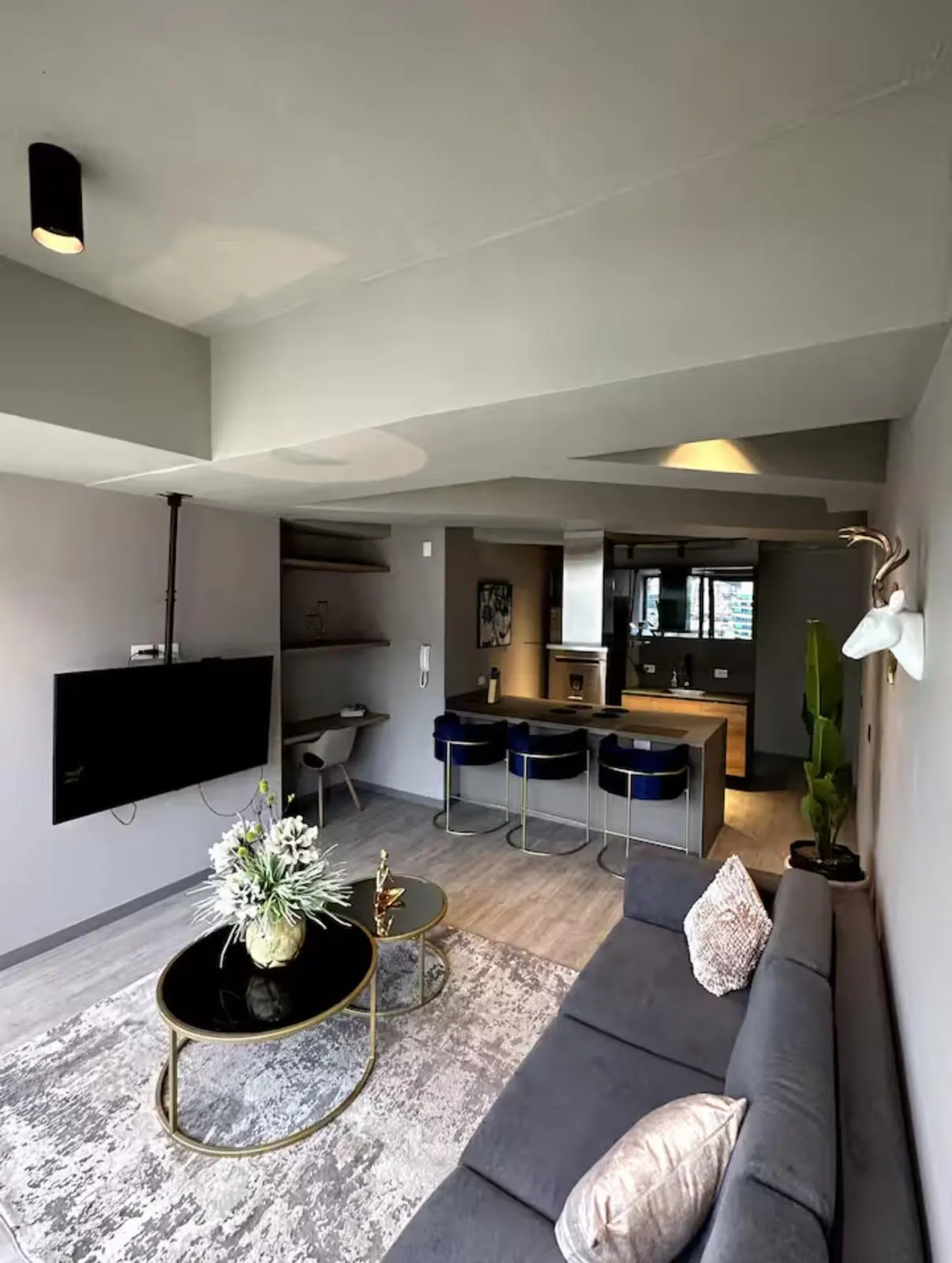 Open-concept living space with gray walls, a dark gray sofa, and a black TV mounted on the ceiling. A kitchen island with blue bar stools is visible.