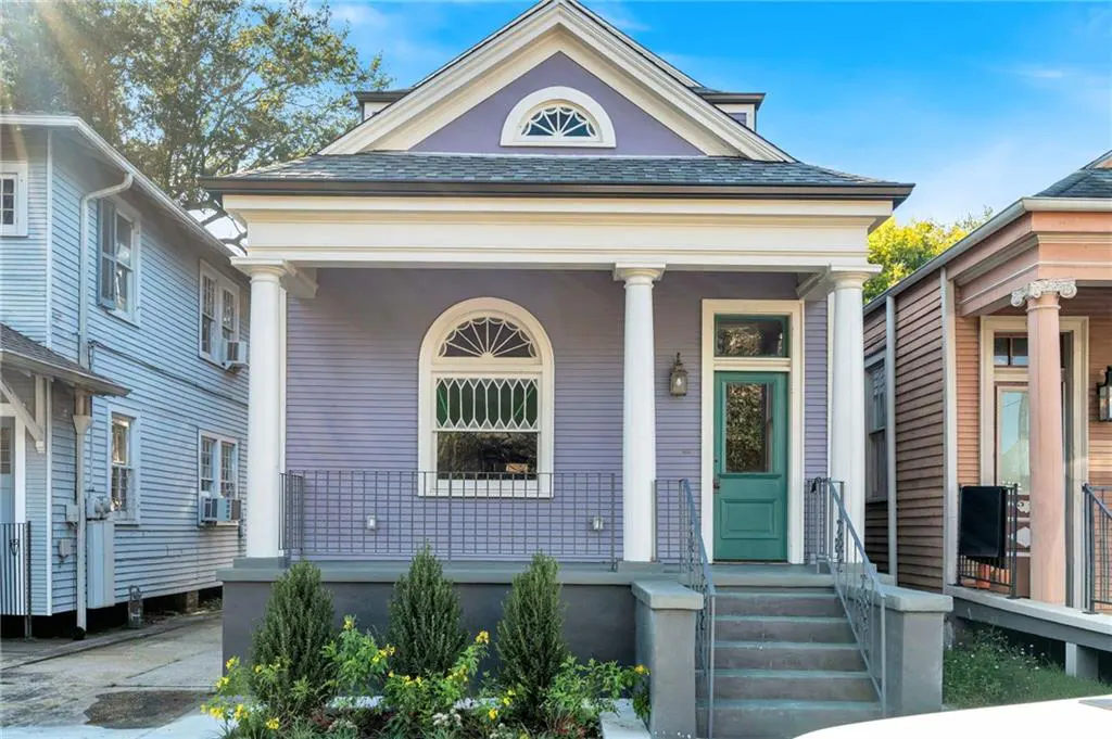A lavender house with white columns and a green door, showcasing classic architecture.