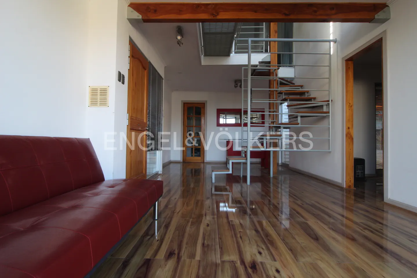 Living room with a red couch, wooden floors, and a metal staircase leading to a second floor.