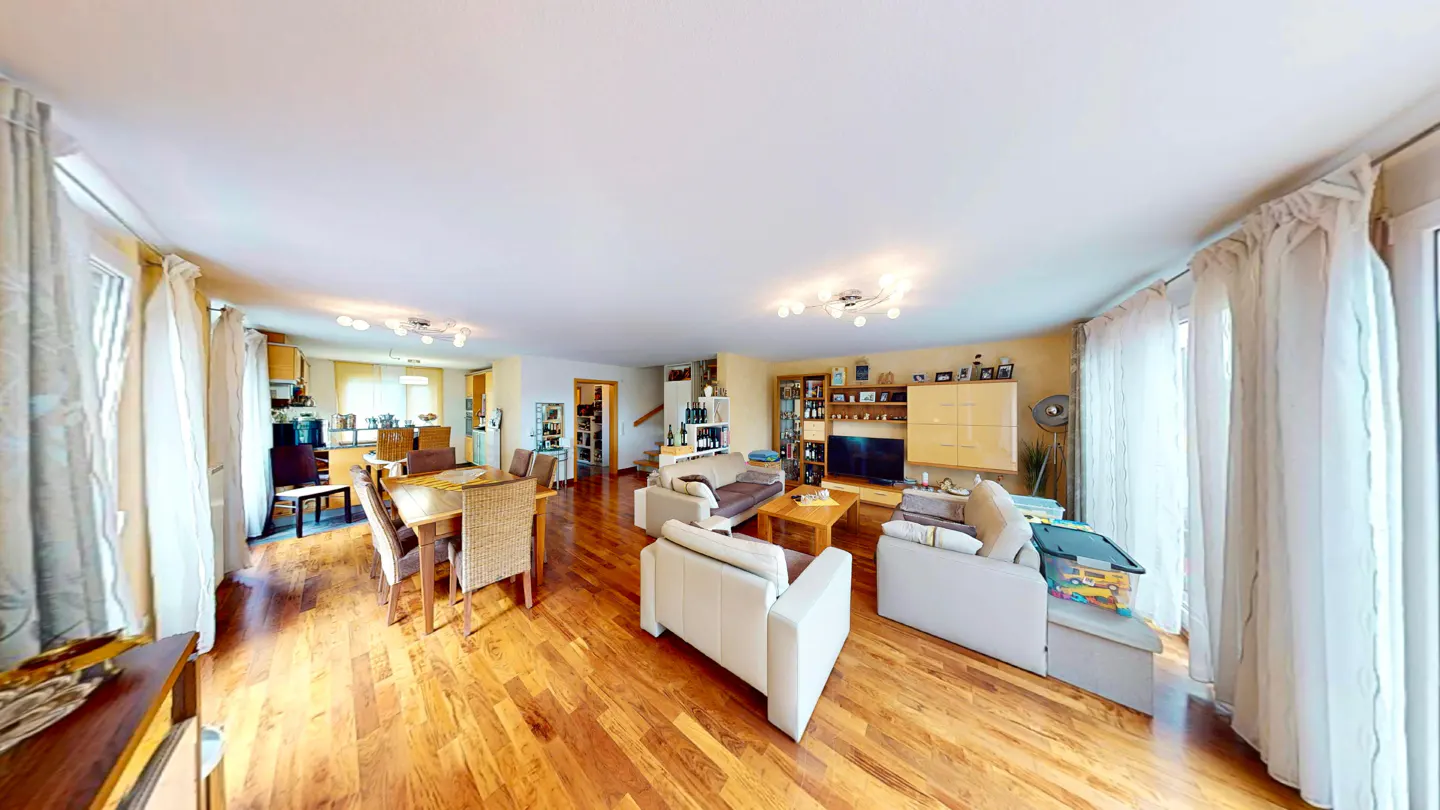 A panoramic view of a living room with hardwood floors, white sofas, a dining table, and a TV.