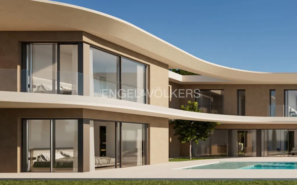 Modern two-story beige villa with curved architecture, floor-to-ceiling windows, and a swimming pool against a blue sky.