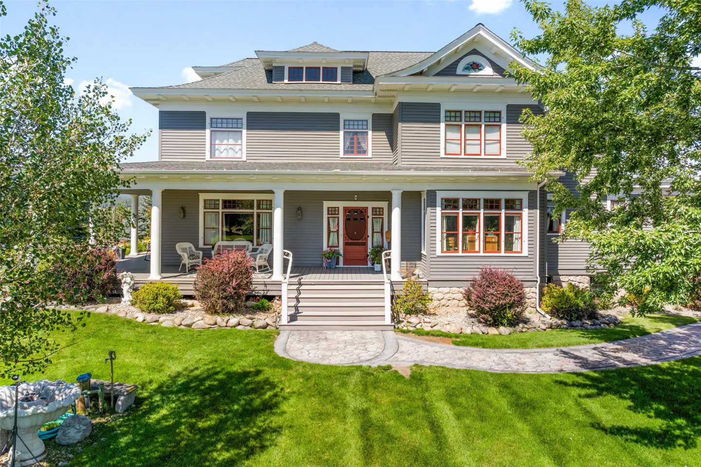 Two-story gray house with white trim, a red door, and a porch with white columns. A stone path leads to the house.
