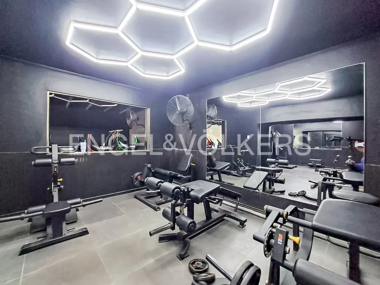 A home gym with black walls, gray floors, and hexagon ceiling lights. Weight machines and a mirror line the walls.