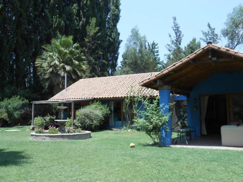 Exterior of a blue house with a terracotta tile roof and a green lawn with a fountain.