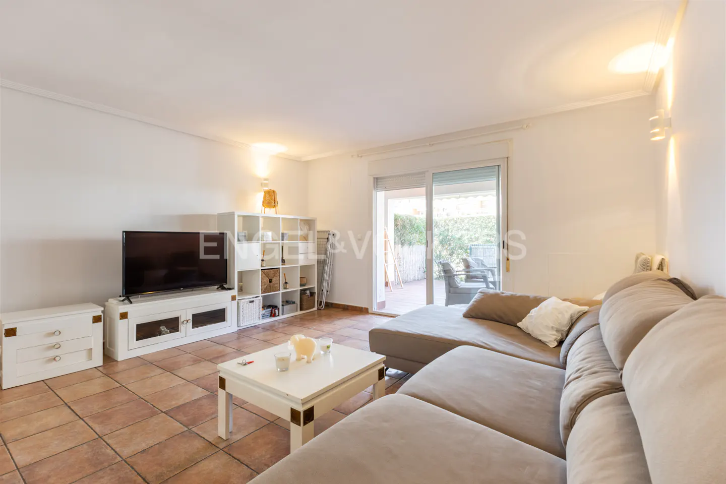 Living room with a large beige sectional sofa, white shelving unit, TV, and a sliding glass door to a patio.