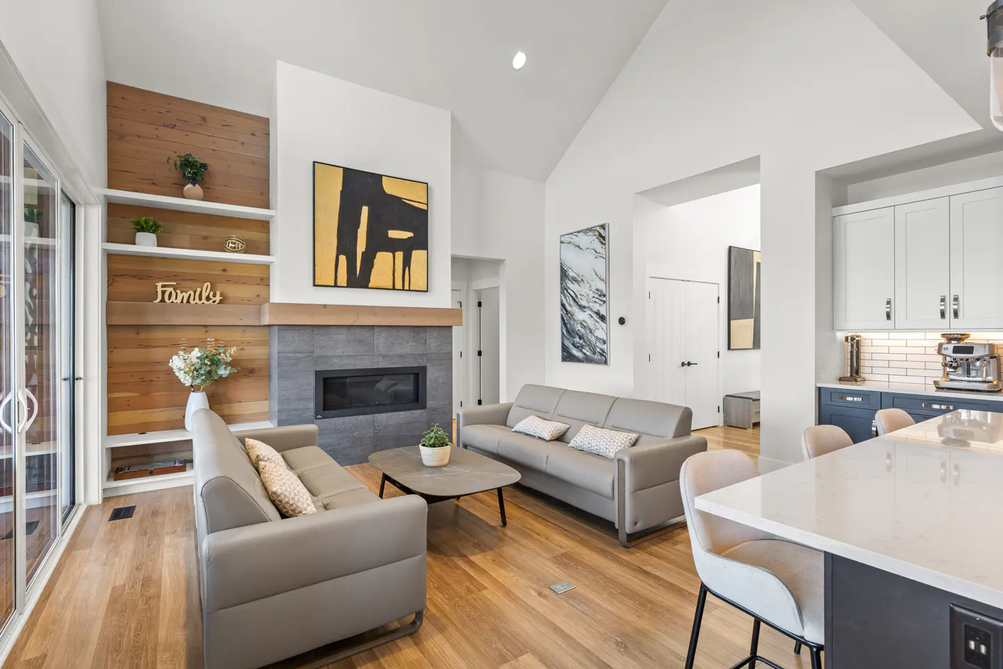 Bright, open-concept living room with gray sofas, wood floors, and a modern fireplace. White walls and wood accents create a warm, inviting space.
