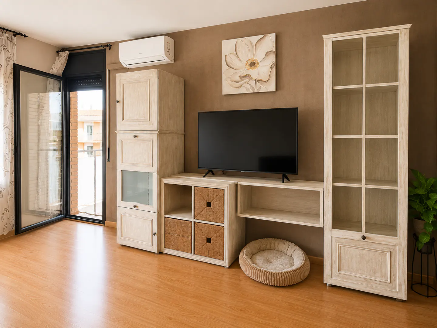 Living room with light wood floors, brown walls, and a black-framed glass door to a balcony. A TV sits on a white media center.