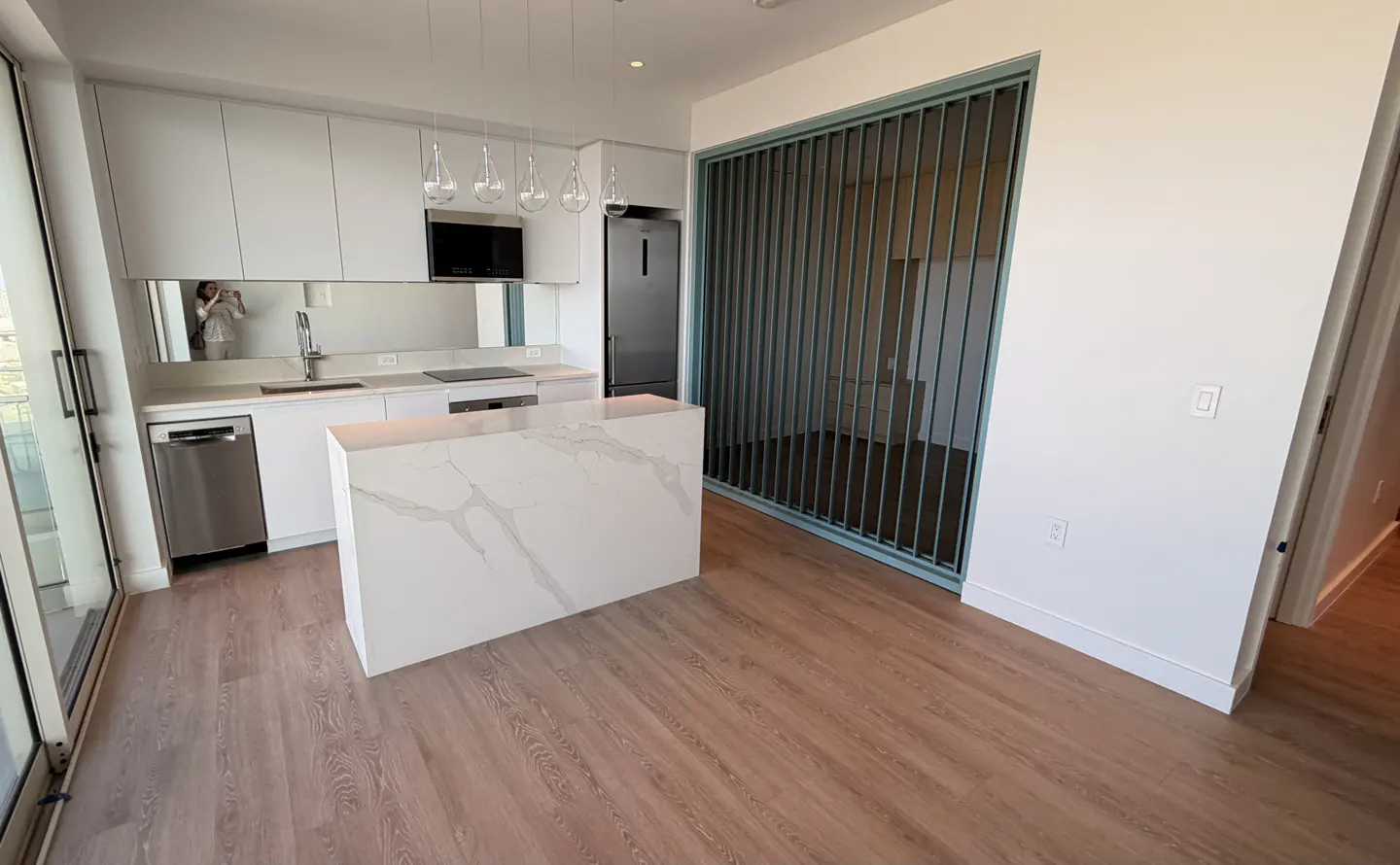 A modern kitchen with white cabinets, stainless steel appliances, and a marble island. A blue metal screen separates the kitchen from another room.