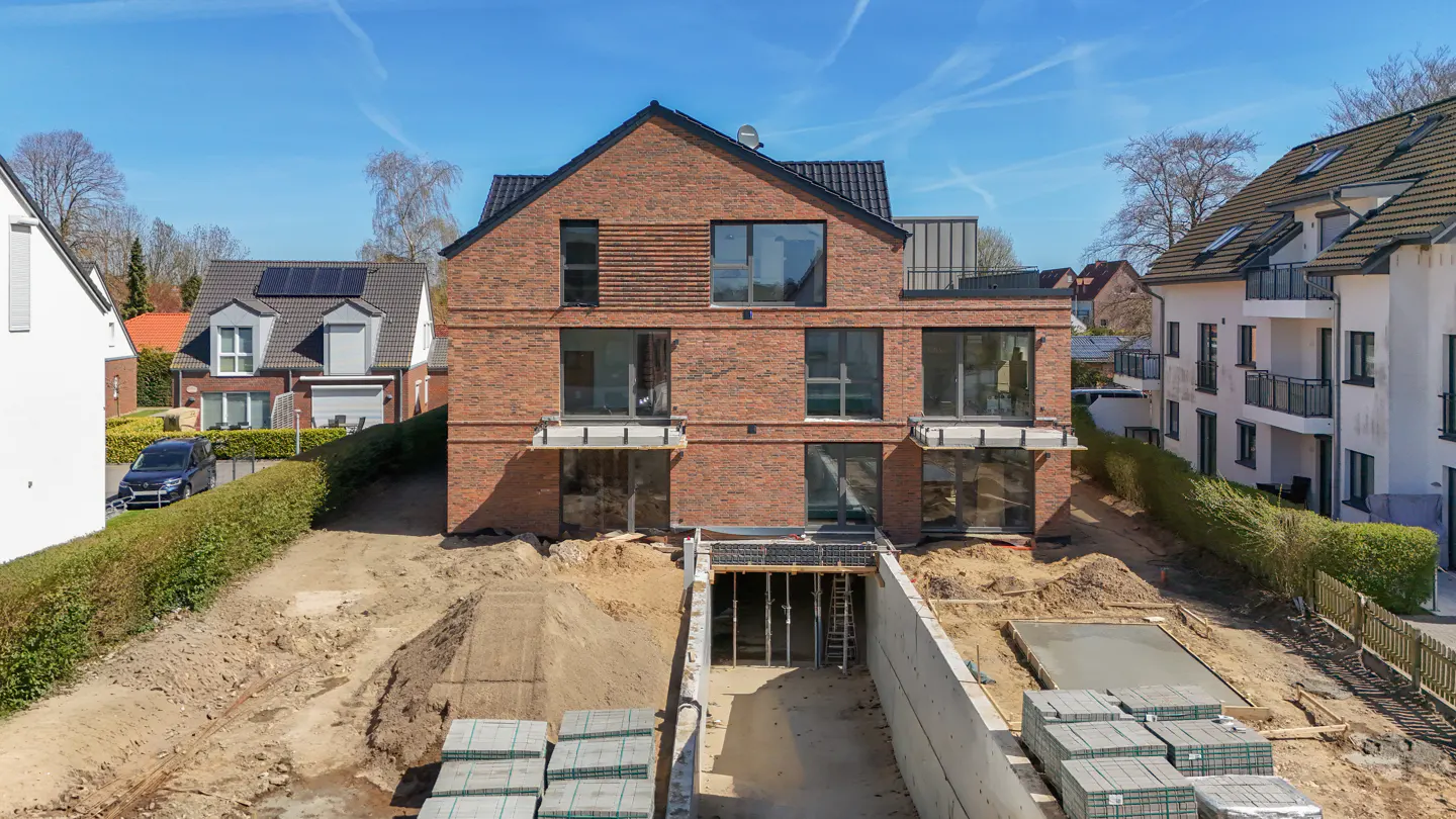 A three-story brick house under construction with a visible basement foundation and building materials.