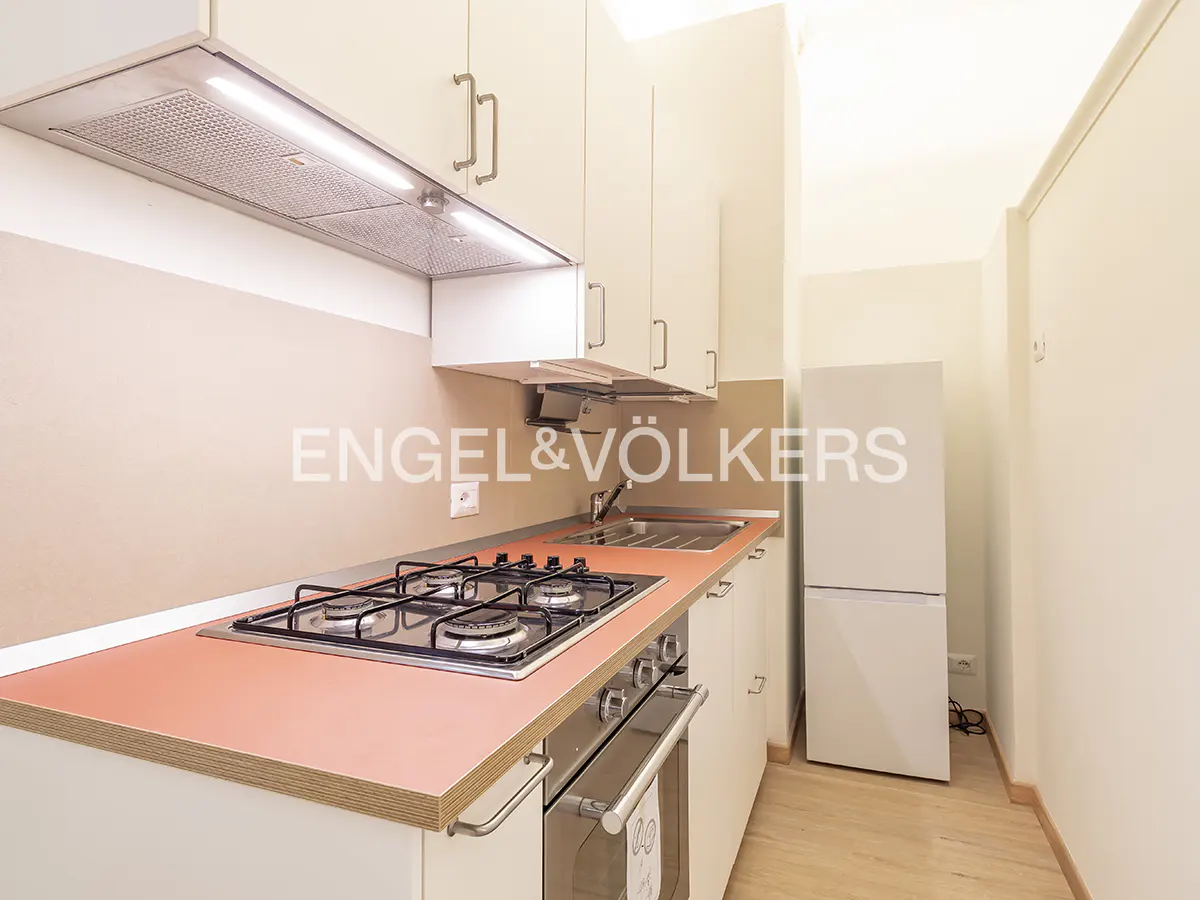 A compact kitchen with white cabinets, a red countertop, and a stainless steel gas stove. A white refrigerator stands against the wall.