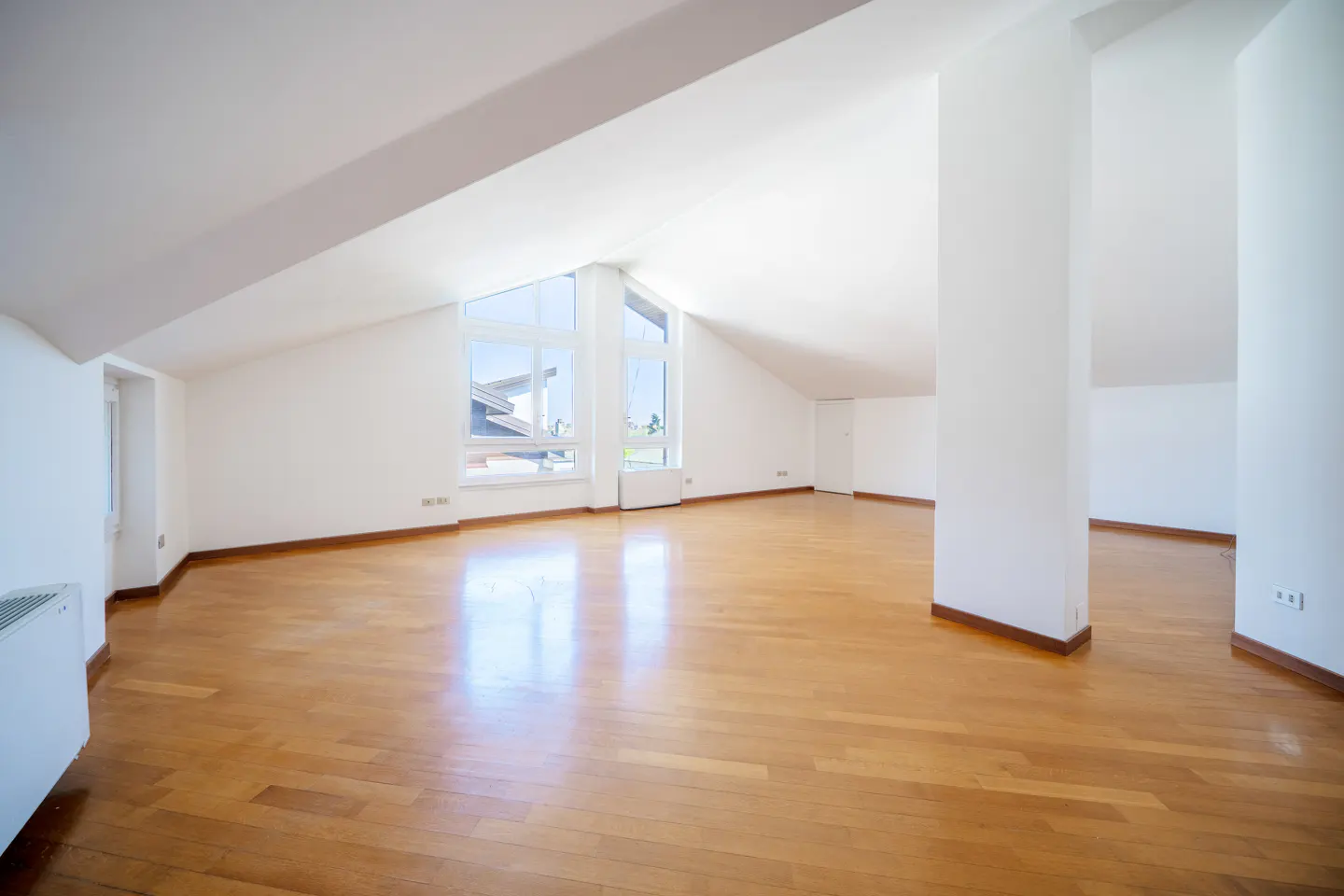 Bright, empty attic room with hardwood floors, white walls, and large windows.