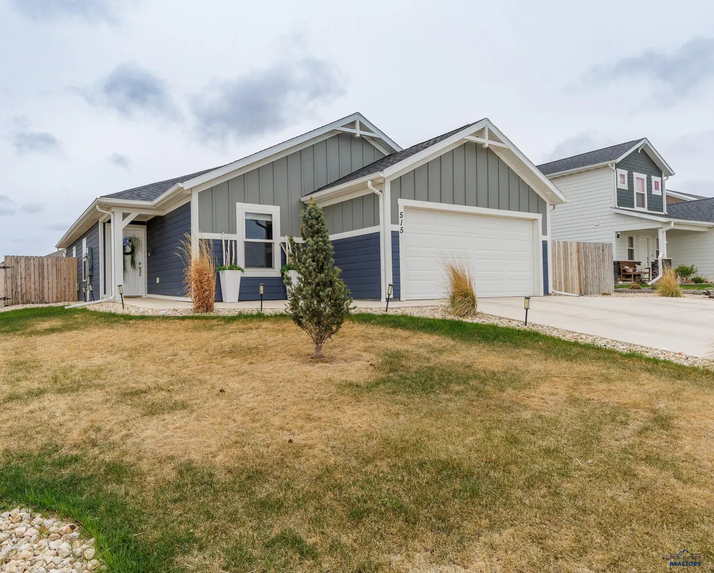 A two-story house with blue and gray siding, a white garage door, and a brown lawn.