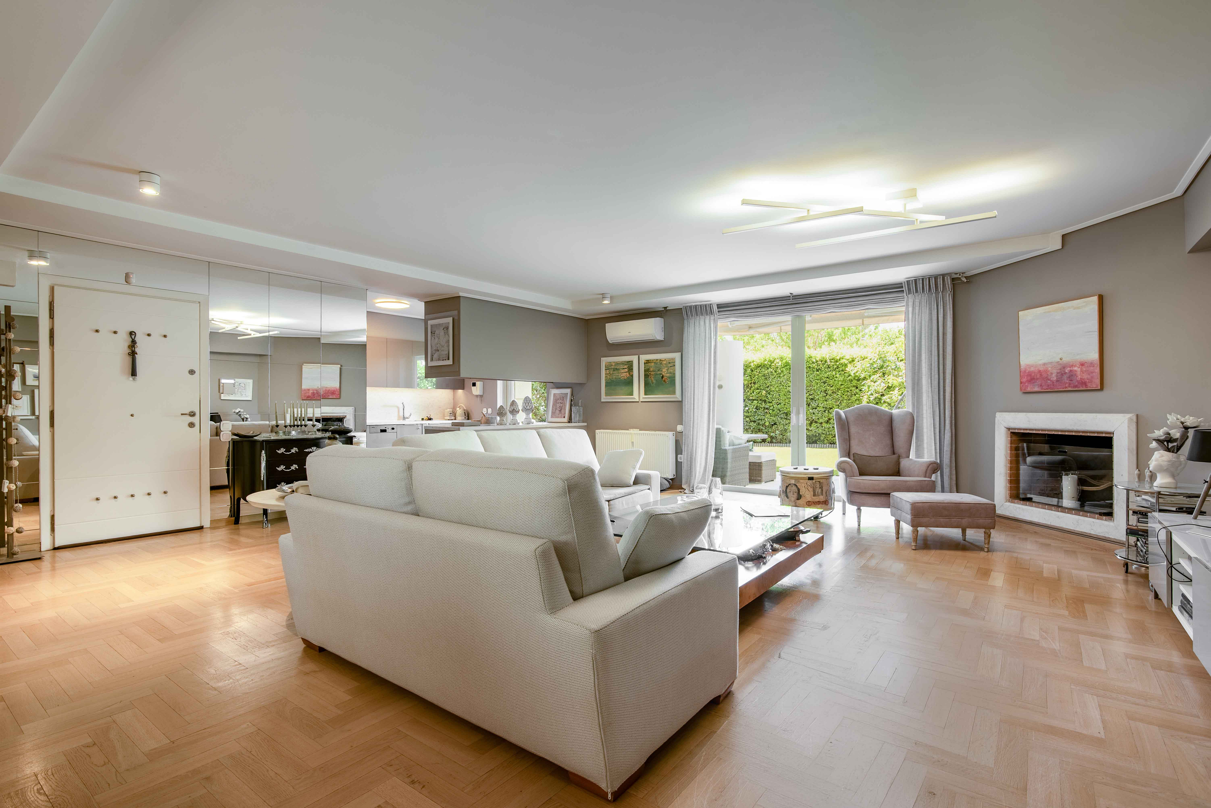 Bright, open living room with white sofa, herringbone wood floor, fireplace, and sliding glass doors to a green yard.