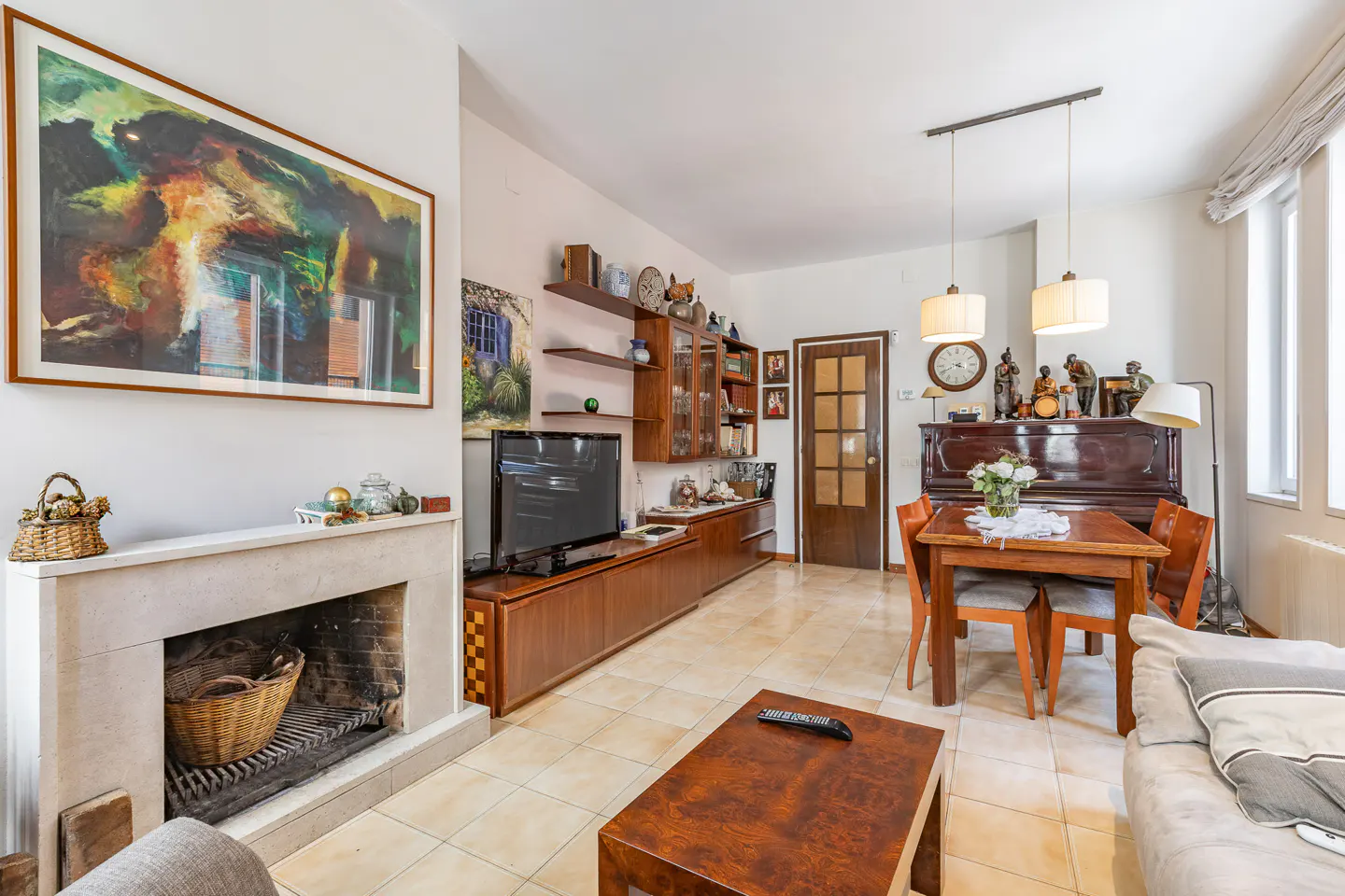 Living room with a stone fireplace, wooden media console, dining table with chairs, and a piano on a tiled floor.