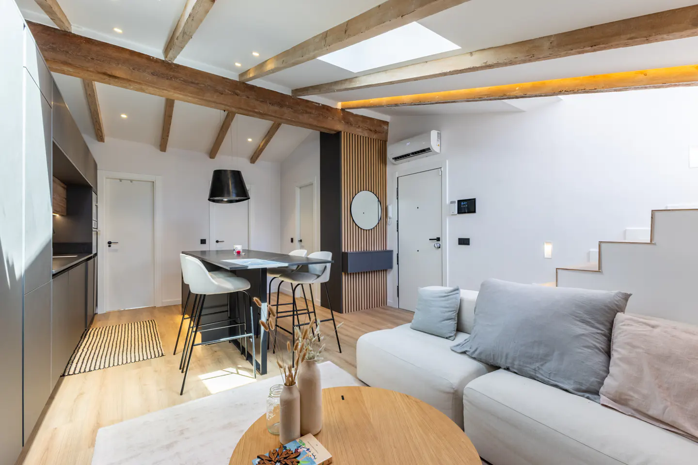 Bright, modern apartment interior with white walls, wooden beams, a kitchen island, and a white sofa.