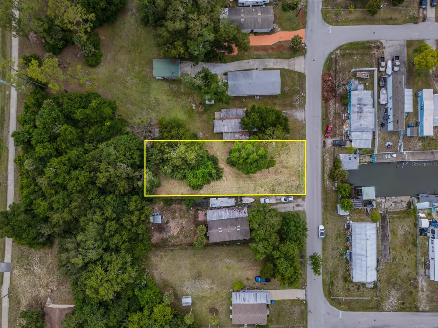 Aerial view of a vacant lot outlined in yellow, surrounded by trees and houses in a residential neighborhood.