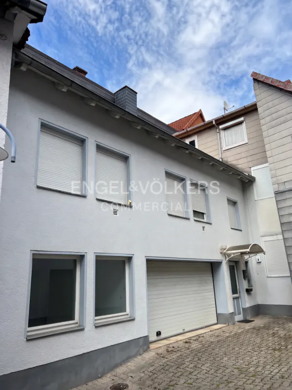 Exterior of a light blue two-story building with a garage and Engel & Völkers logo. Blue sky with clouds above.