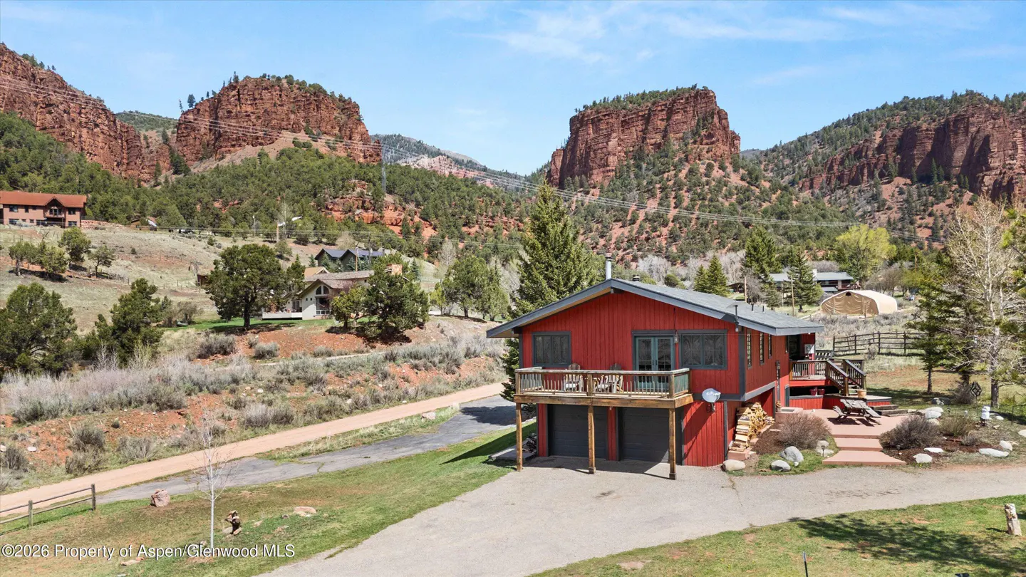 Exterior view of a red two-story house with a garage, deck, and red rock mountain backdrop.
