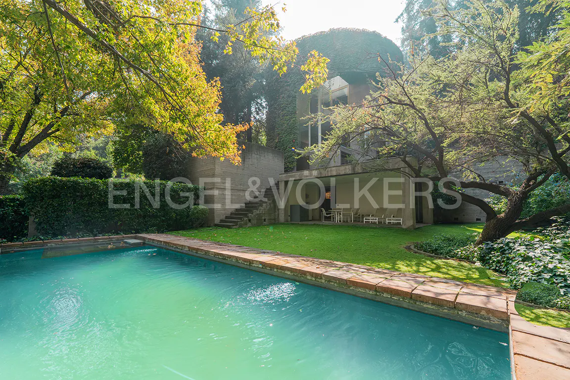 A backyard with a turquoise pool, green grass, and a modern house with stone stairs and an Engel & Volkers logo.