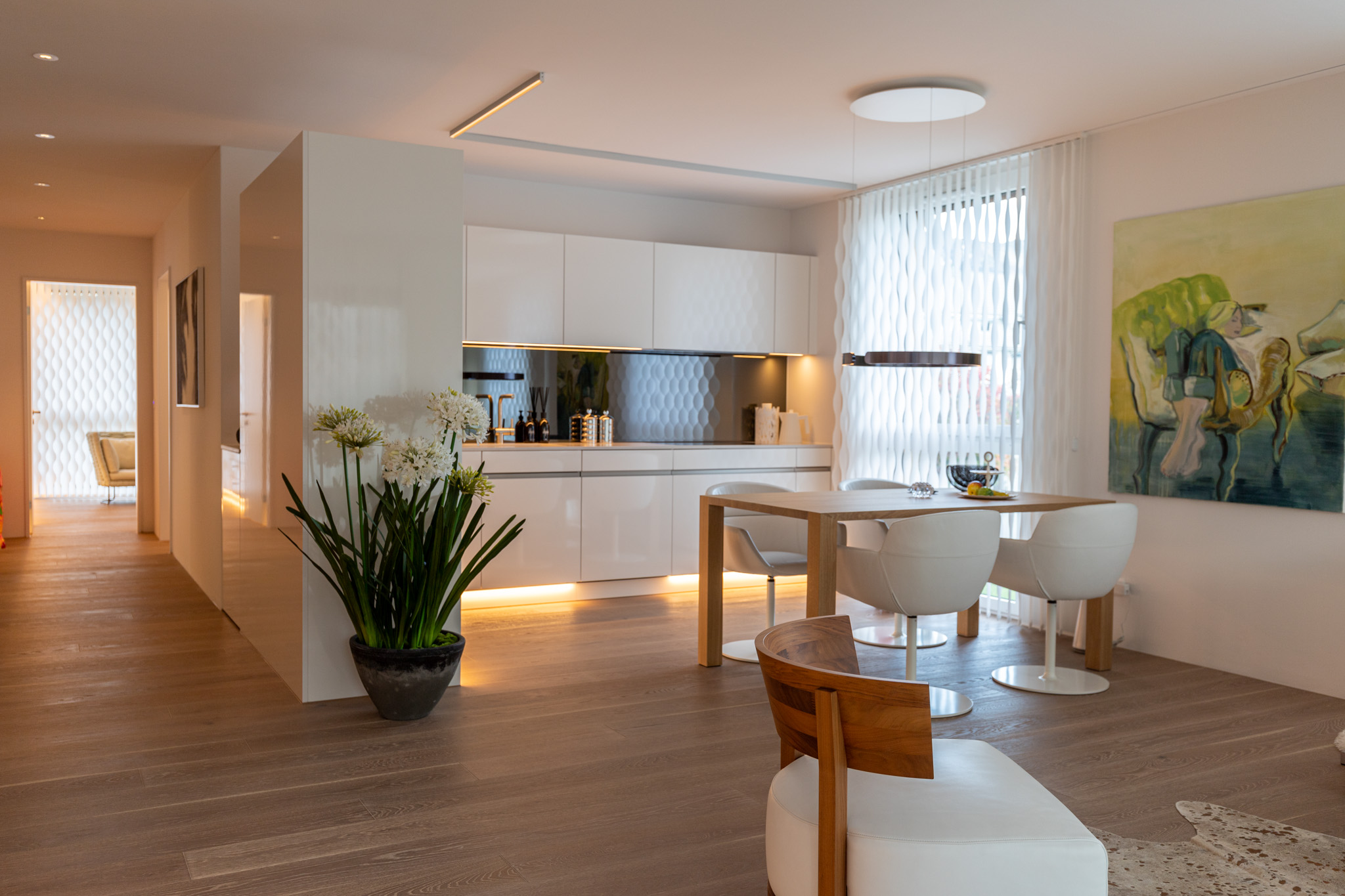 Modern open-plan kitchen and dining area with white cabinets, wooden floors, a dining table, and abstract wall art.