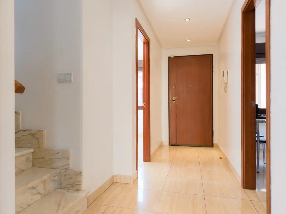 Hallway with marble stairs, beige tile floor, white walls, and brown doors.
