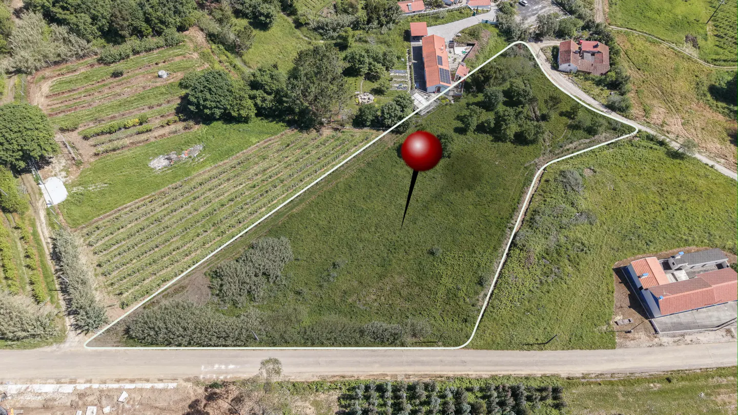 Aerial view of a grassy lot outlined in white, with a red pin marking a spot. Farmland and houses are in the background.