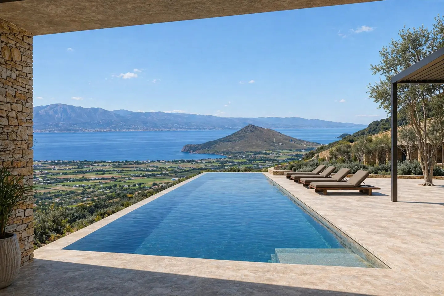 Infinity pool overlooking a blue sea and green landscape. Four lounge chairs sit on the stone patio.