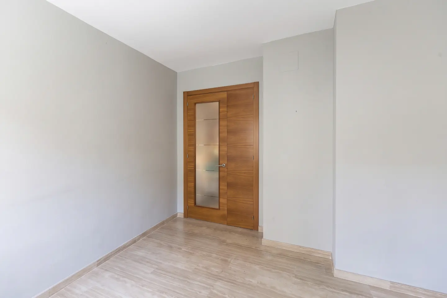 Empty room with light gray walls, marble floor, and a wooden door with a frosted glass panel.