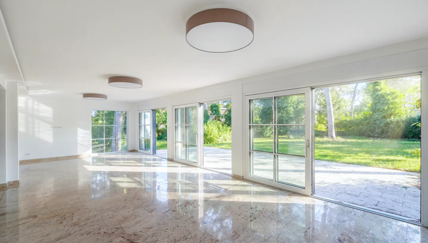Bright, empty room with polished marble floors, white walls, modern ceiling lights, and large glass doors to a garden.