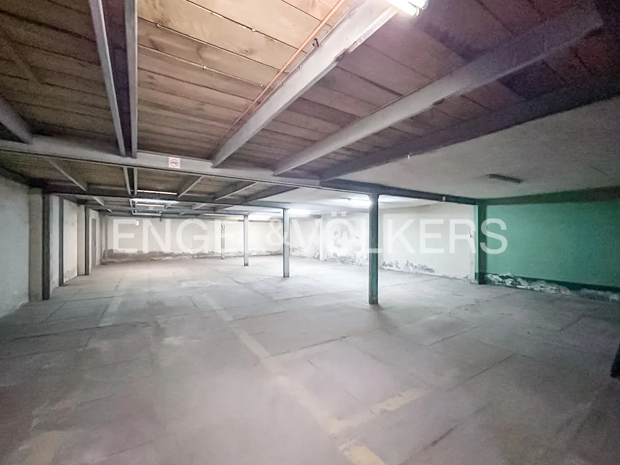 An empty parking garage with concrete floors, support beams, and overhead lighting.