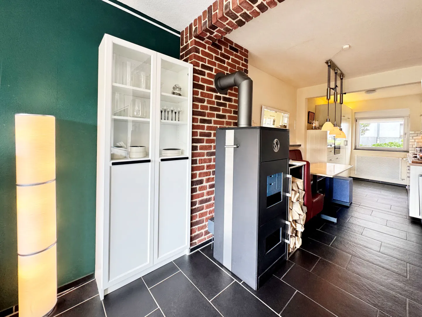 A modern kitchen with a wood-burning stove, white cabinets, and a green wall.