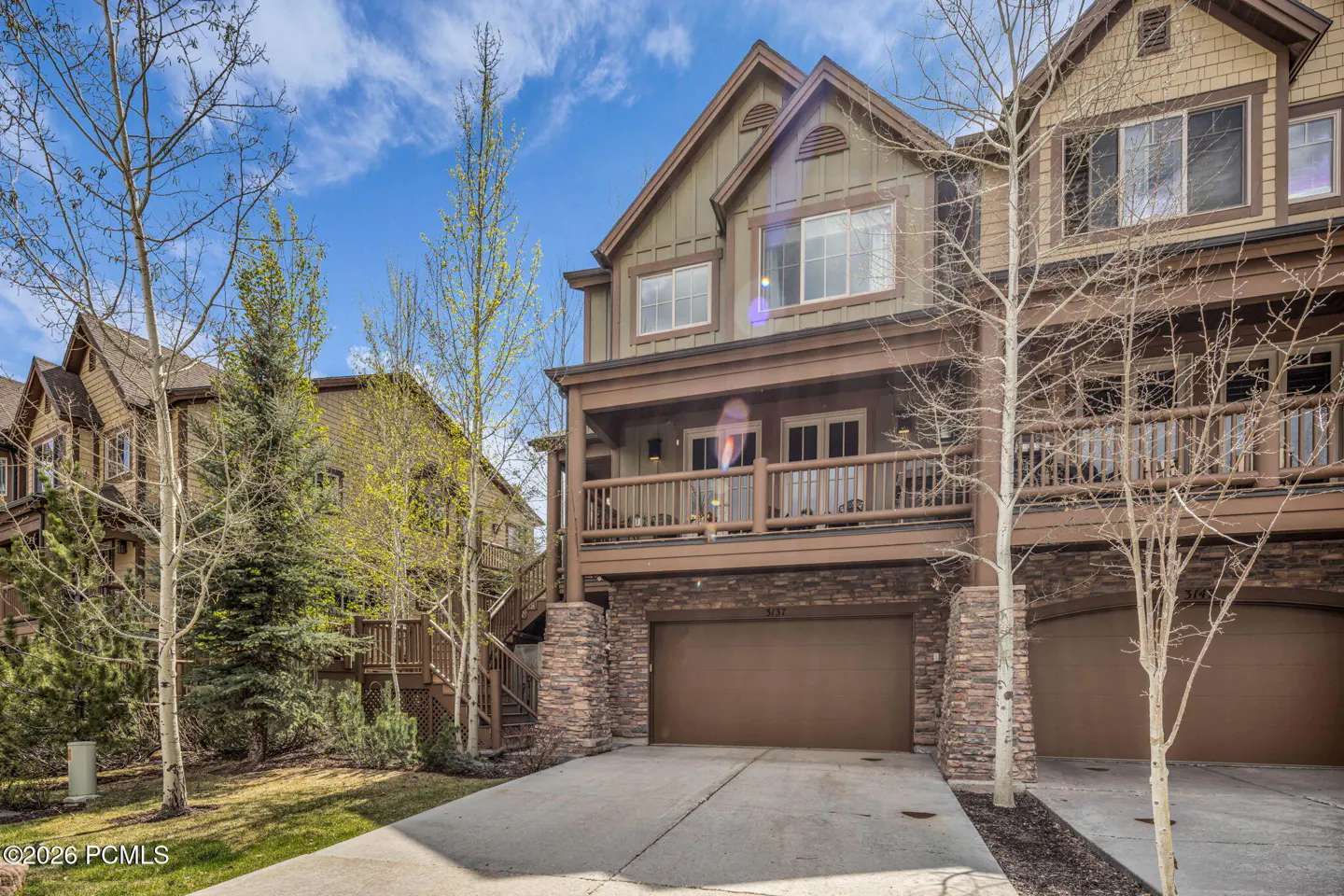 Exterior of a two-story townhouse with a brown garage door and stone accents. Balcony on the second floor. Blue sky.