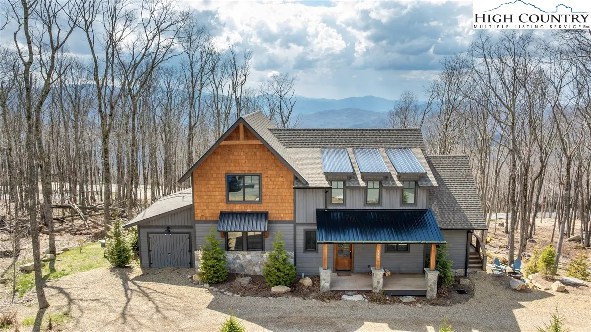 Exterior view of a two-story house with gray siding, brown shingles, and a black metal roof, surrounded by trees.